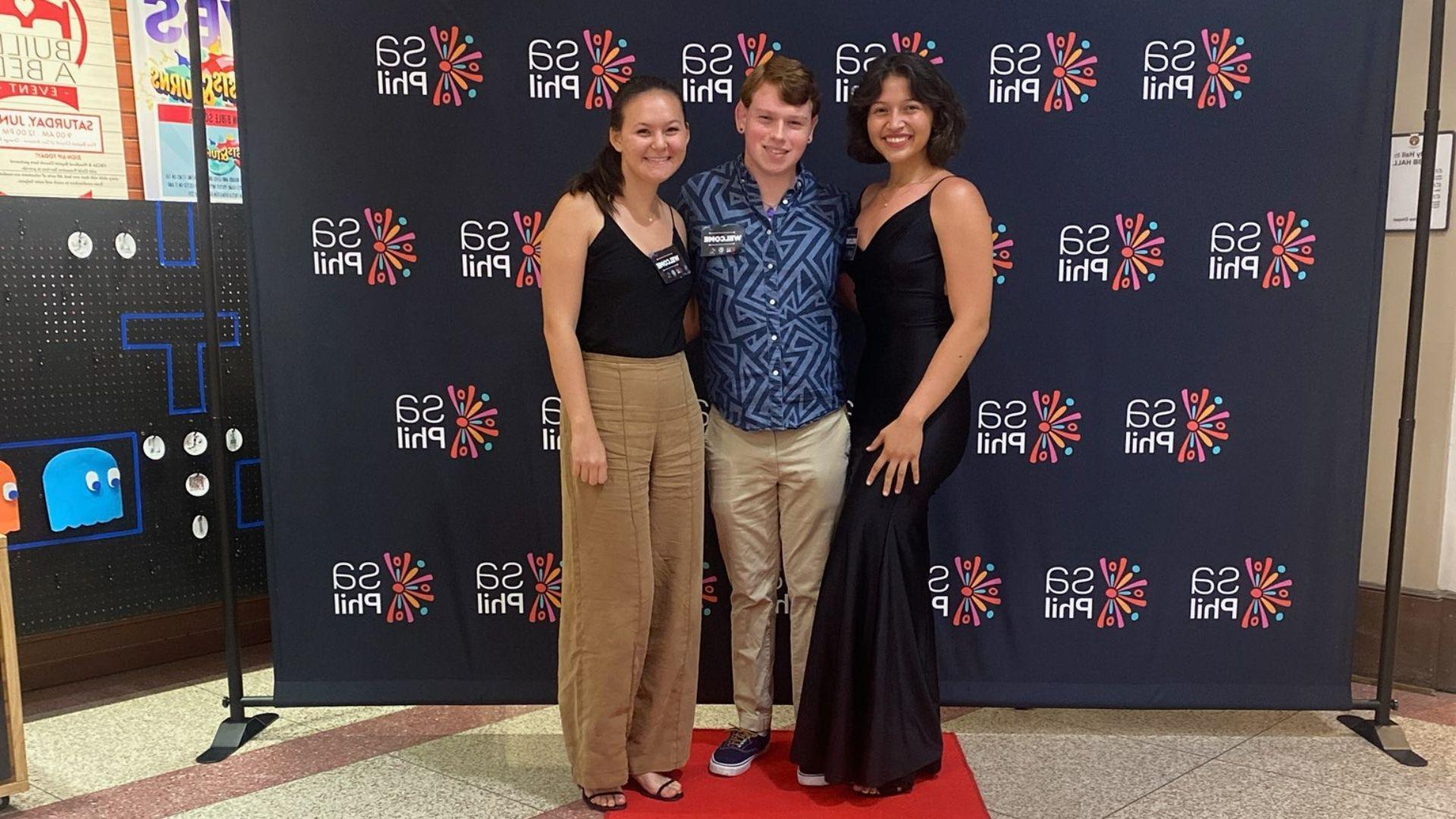 Jake Cipolla (center) poses for a photo with his coworkers at a photo curtain wall at a 圣安东尼奥 Philharmonic concert