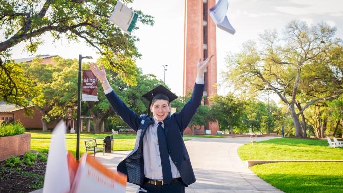 photo of recent graduate outside tossing books in the air 和 smiling