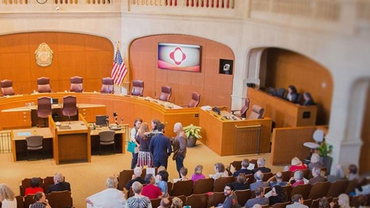 Government officials 和 community members gather together in council room for a hearing.