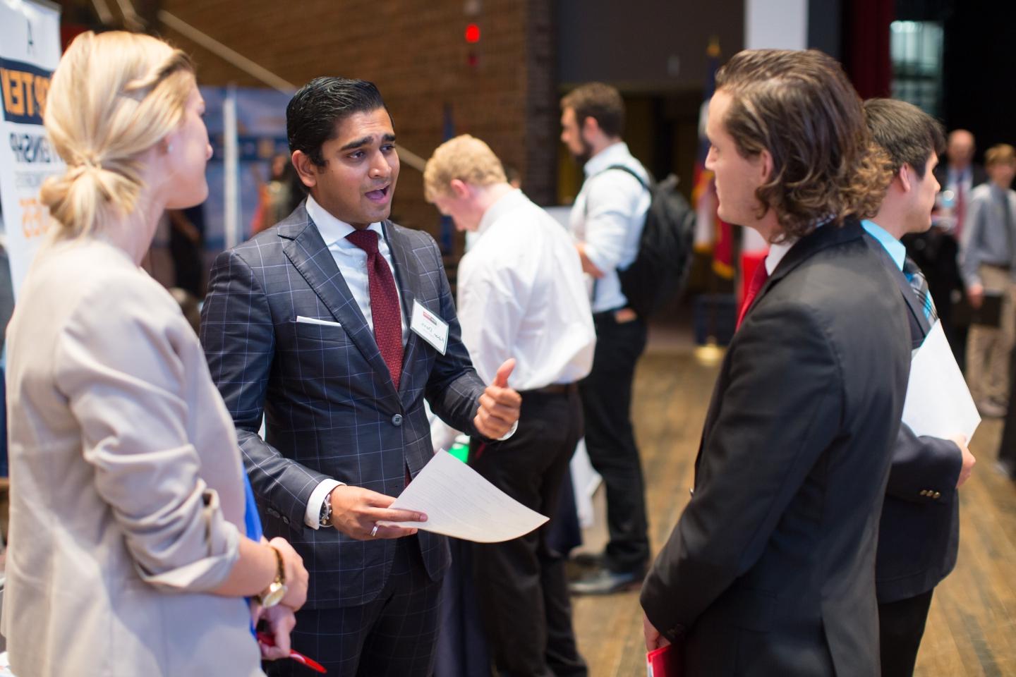 a student in a suit speaks with two potential employers in Laurie Auditorium at a 招聘会